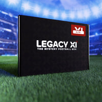 Boîte mystère de maillot de football Legacy XI Elite posée sur la pelouse d'un stade de foot éclairé.