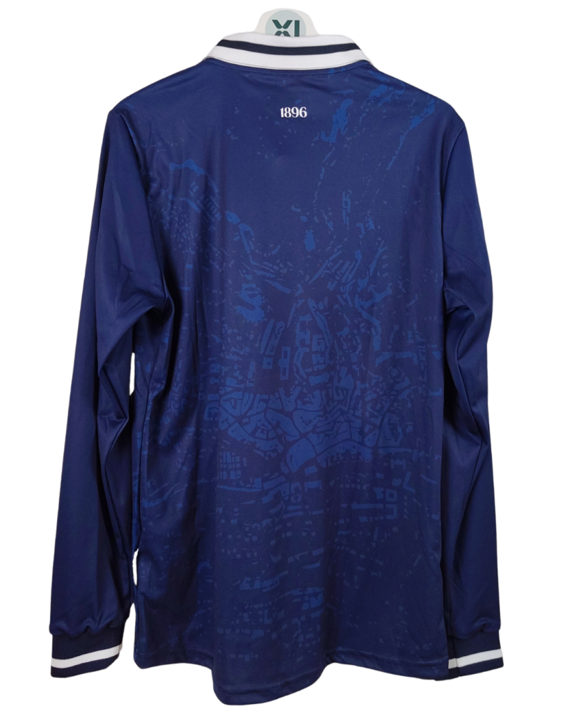 Vue de dos du troisième maillot de football à manches longues 2024-25 du Lausanne-Sport, présenté sur un cintre contre un fond noir. Le maillot est bleu marine avec un motif graphique complexe, ton sur ton, qui ressemble à une carte urbaine stylisée. Le col est un col polo classique avec des rayures blanches et bleu marine sur les bords. Le nombre '1896' est brodé en blanc au centre, juste en dessous du col.