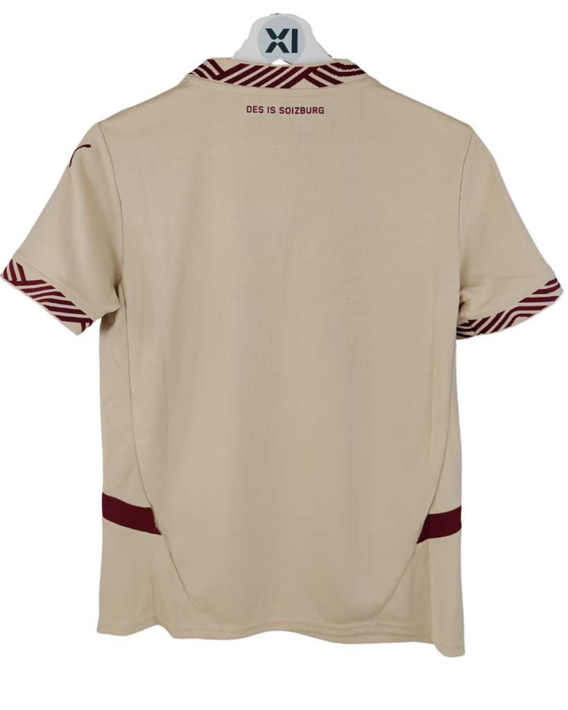 Beige polo shirt shown from the back with maroon striped collar and sleeve trim; text 'DES IS SOIZBURG' on upper back.