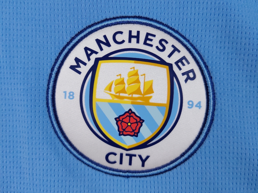 Logo officiel du Manchester City Football Club brodé sur le tissu bleu ciel du maillot.