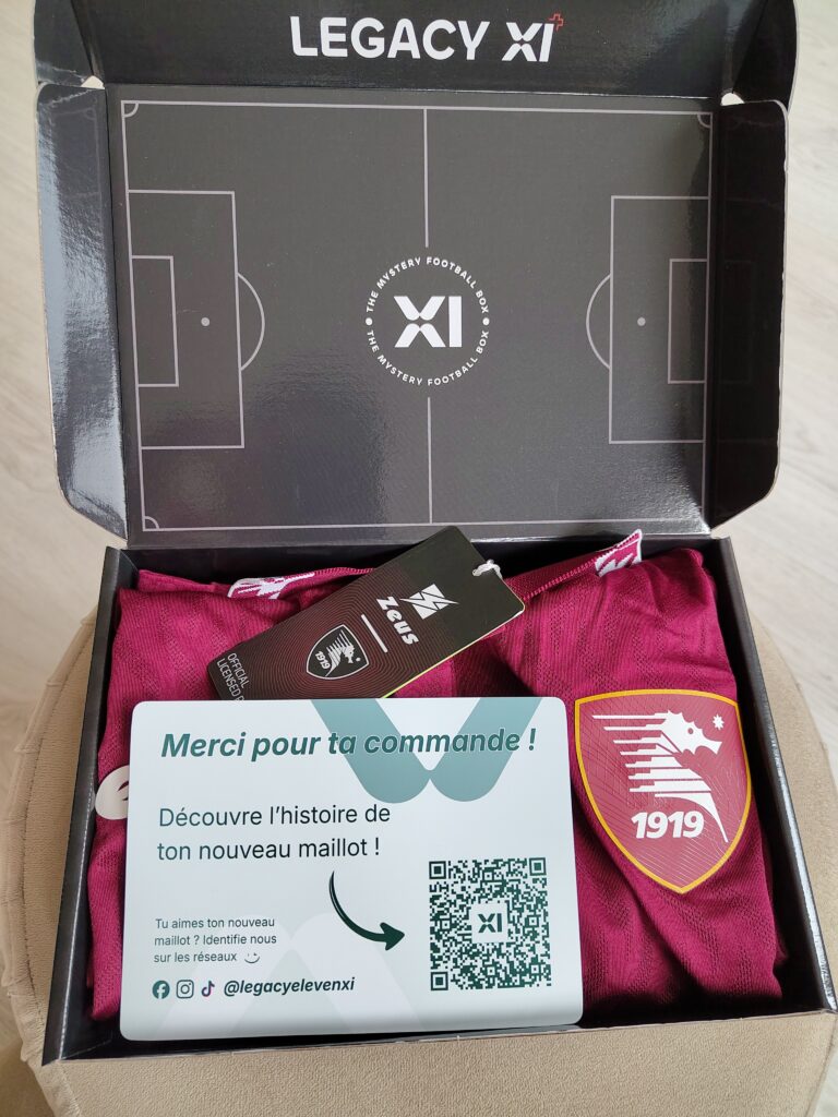 Une boîte ouverte « Legacy XI » contenant un maillot de football bordeaux de l'US Salernitana 1919 et une carte de remerciement posée sur le dessus.