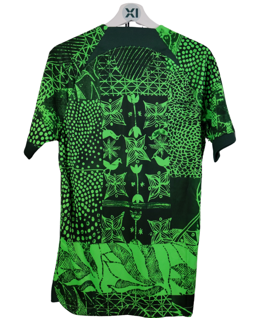 Green and black patchwork short-sleeve shirt on a white hanger, featuring bird and leaf motifs with geometric patterns.